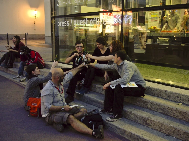 a group of people sitting down on the steps in front of a glass window