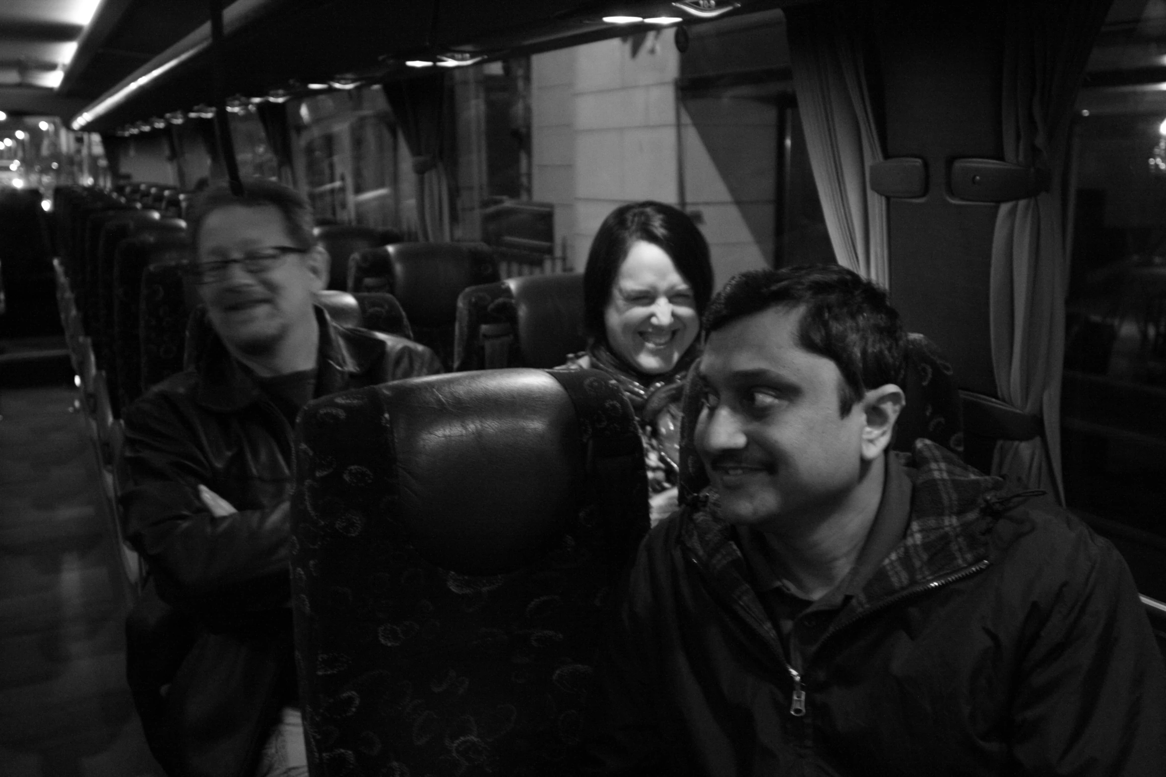 three people smile while sitting on a bus