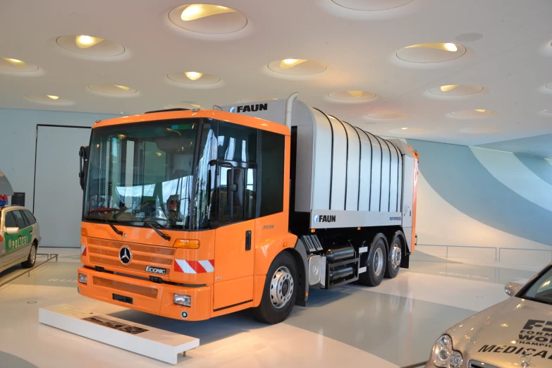 orange semi truck parked in a showroom surrounded by other vehicles