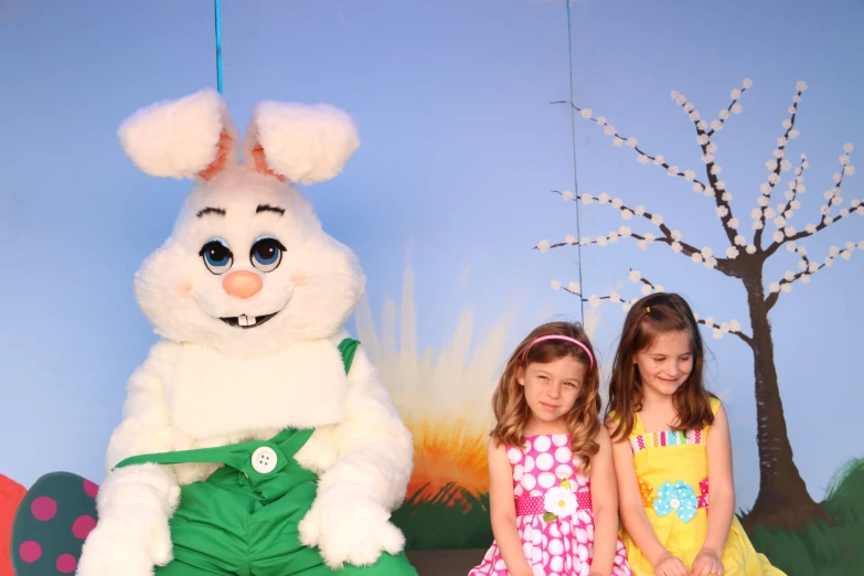 two girls sitting in front of a big easter bunny