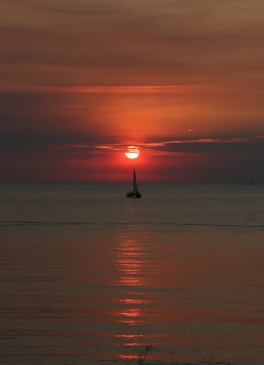 the sun setting in front of a sail boat on the water