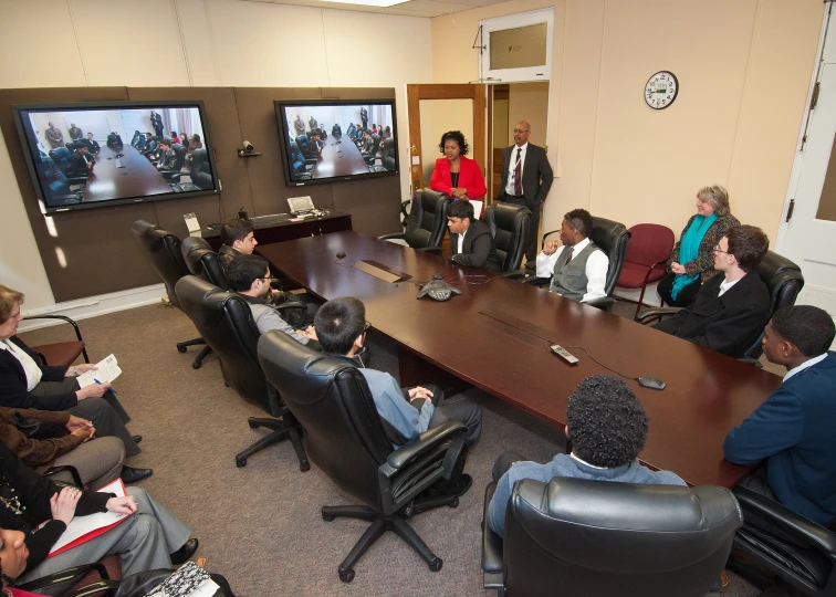 several people sit in chairs while watching two televisions in the background