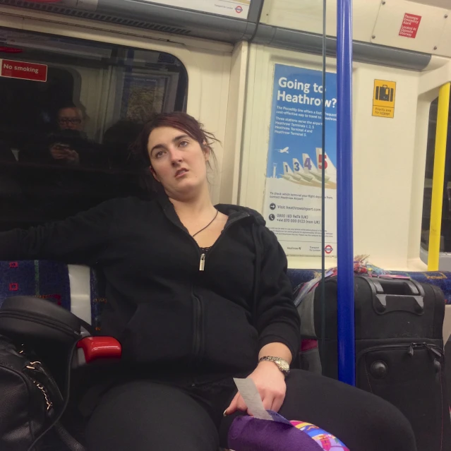 woman wearing a black sweatshirt and black pants sits on the subway