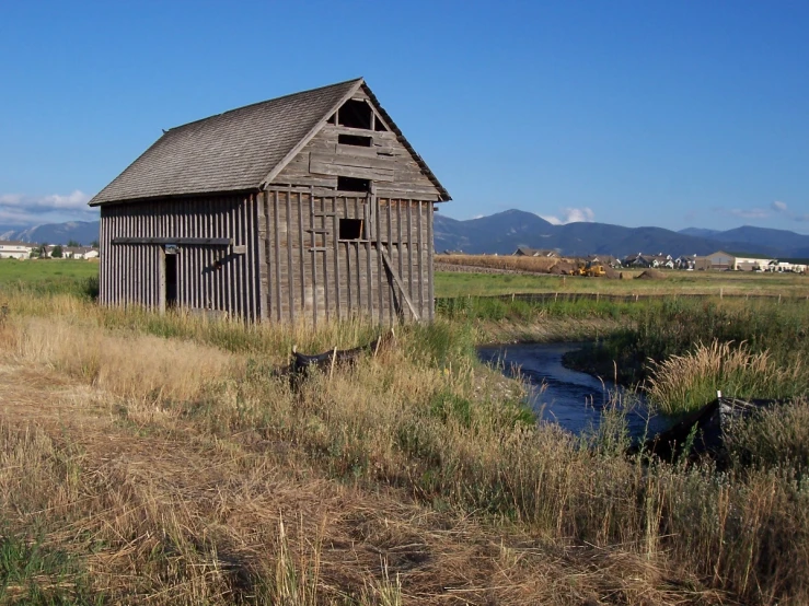 an old barn sits in a grassy field with water flowing