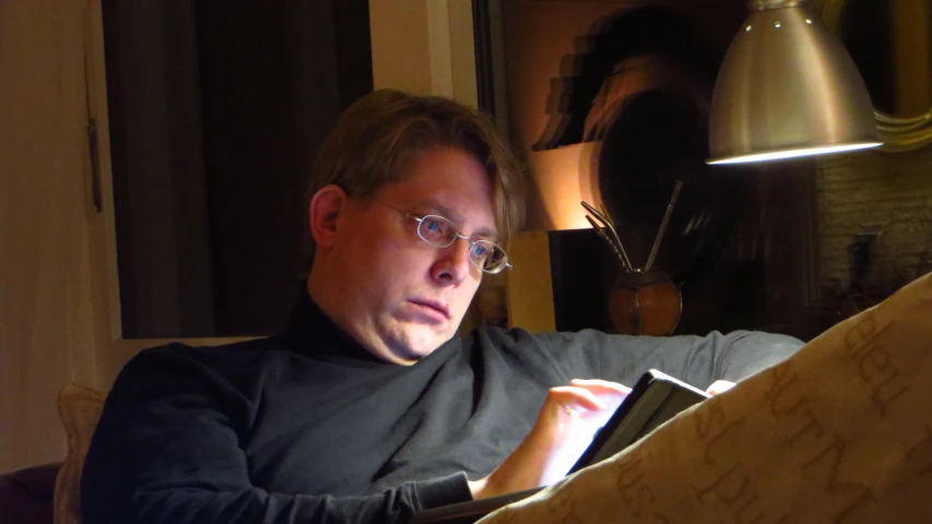 man sitting in chair with newspaper while looking at laptop