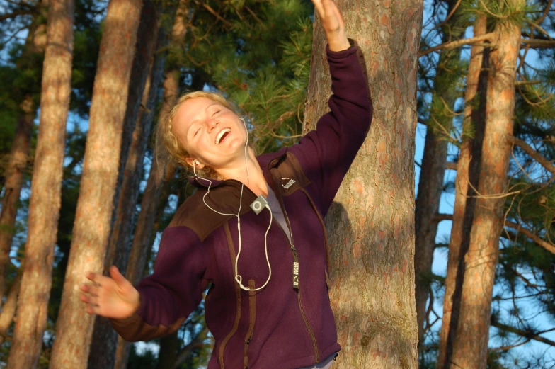 a woman reaching up to the sky near some trees