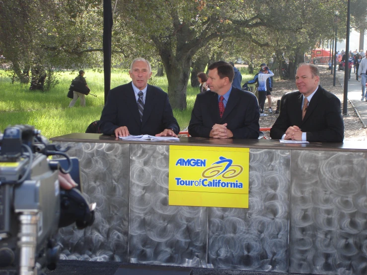 three men in suits sitting at a table in front of an awning