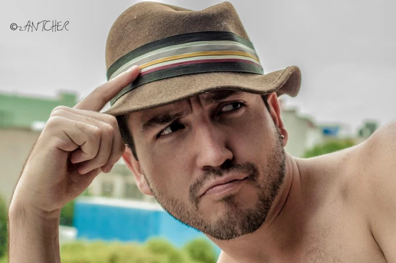 a shirtless man with a brown fedora standing outside