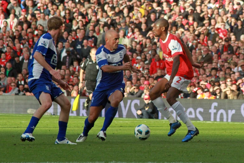 men playing soccer, one chasing the ball while another is blocking