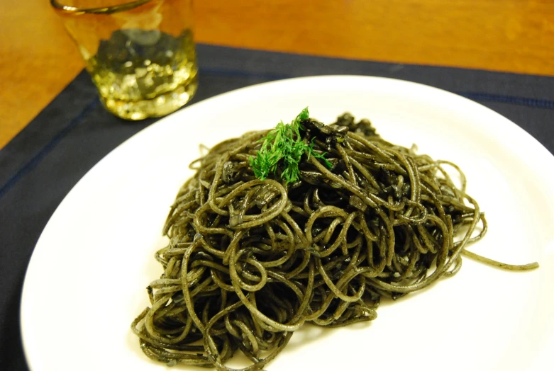 a plate with a green pasta dish and a glass of water