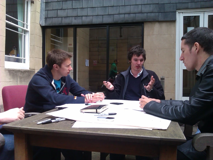 several men sit at a table together in front of a house