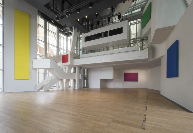 an open white room with a staircase, some colors of painting and windows