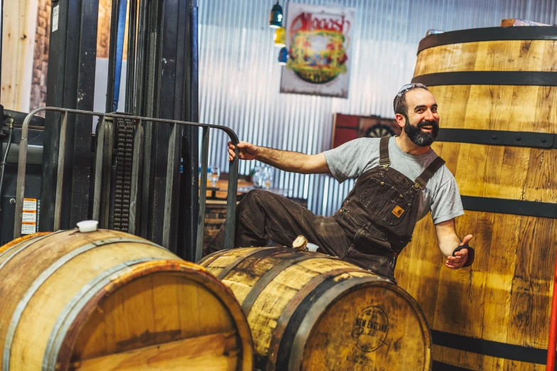 a man with a beard sitting on the top of two wooden barrels