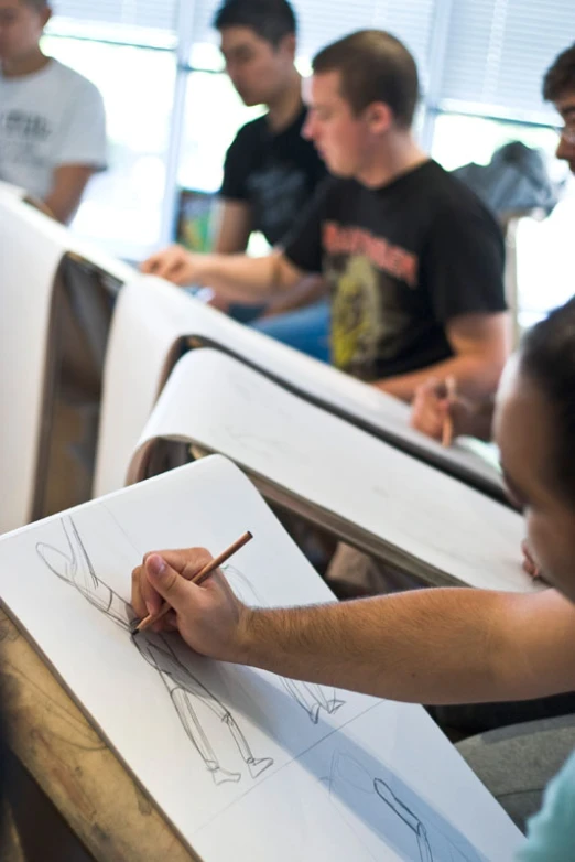 several young men drawing drawings with pens on paper