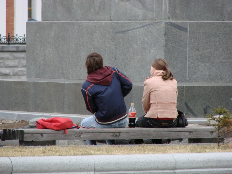 there are two people sitting on a bench near a statue