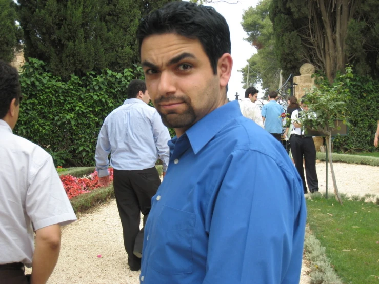 a man in blue shirt standing next to a bush with trees