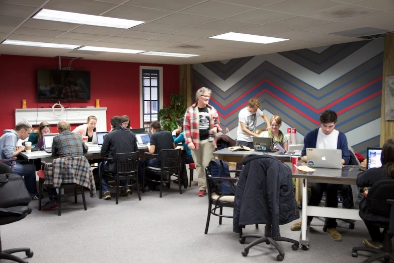 an office filled with students sitting at desk and looking at laptops