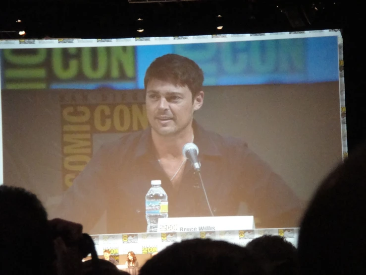 a man standing behind a microphone with a big screen in front of him