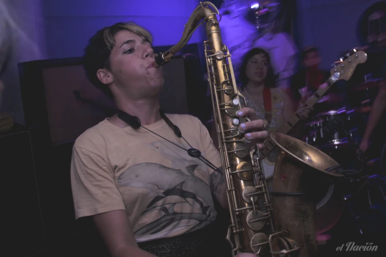 the person is playing the saxophone with other people behind him