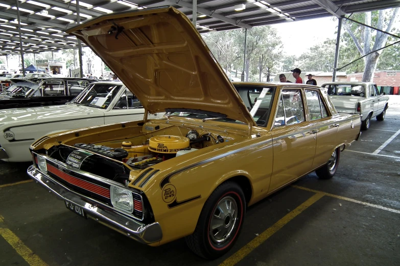 old yellow and black car parked in a lot next to older white cars