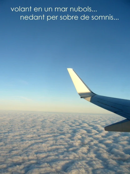 a white airplane wing flying in the sky above clouds