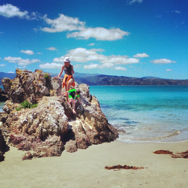 a woman is sitting on the edge of rocks near the ocean