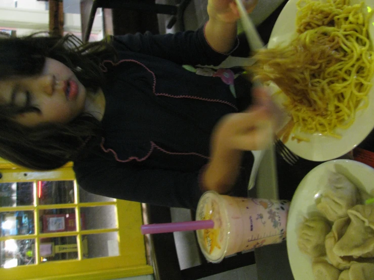 the child is sitting down to eat some noodles