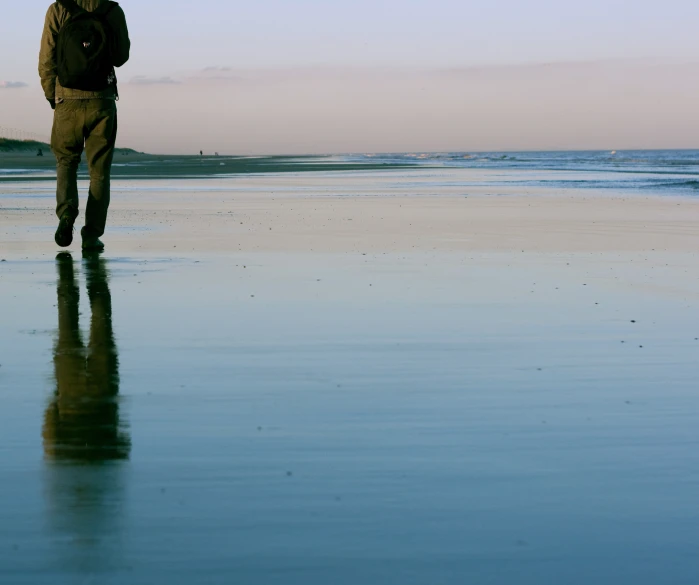 a man walking along a wet beach with a surf board