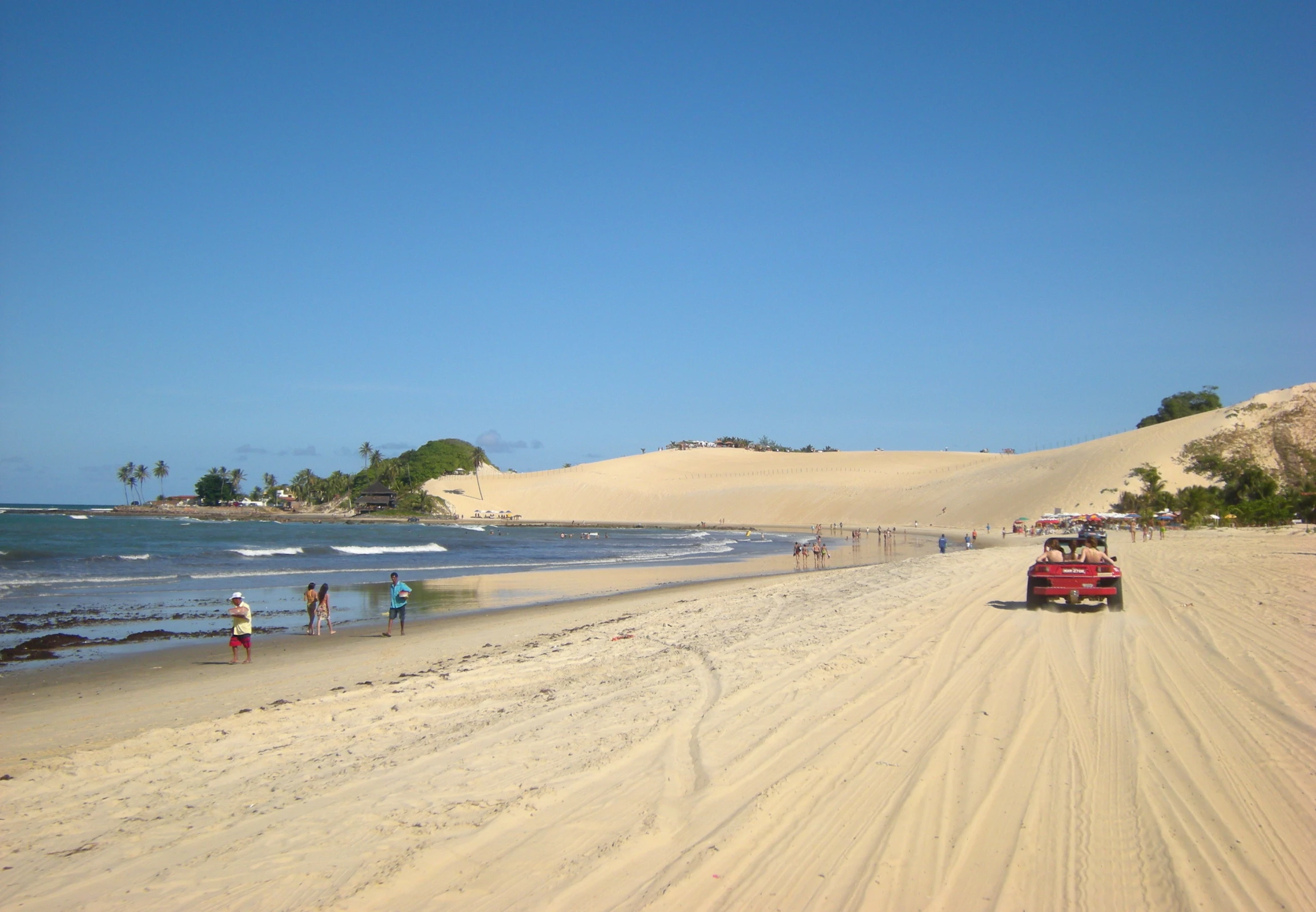 people walking on the beach next to a truck