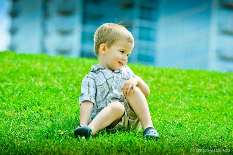 a little boy sitting in the grass near a building