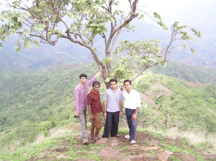 three people standing on top of a mountain next to a tree