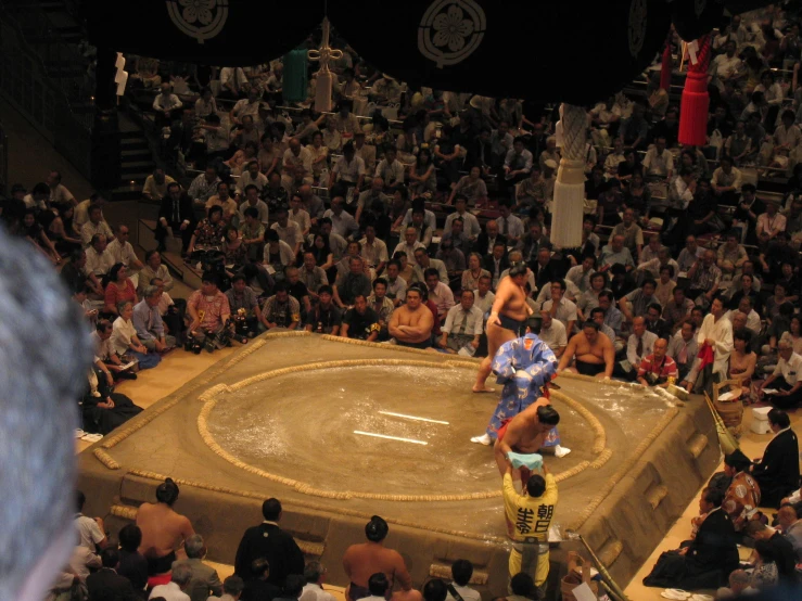 a group of people standing around a ring with a sumo wrestler on it