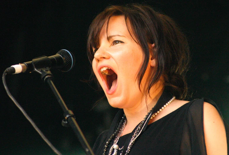 an asian woman singing on a microphone with her mouth open