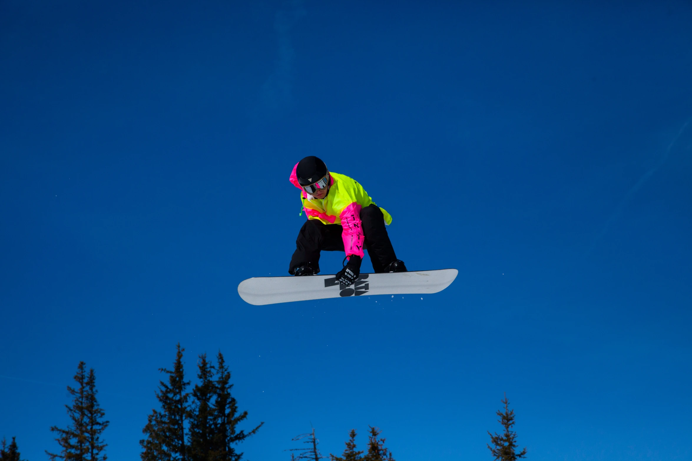 a snowboarder in neon colored jacket jumping through the air