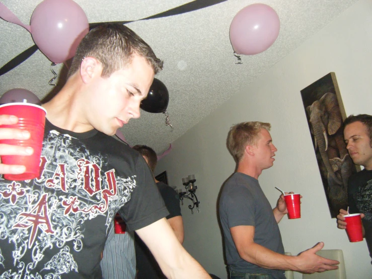 a group of men in room with balloons and a red cup