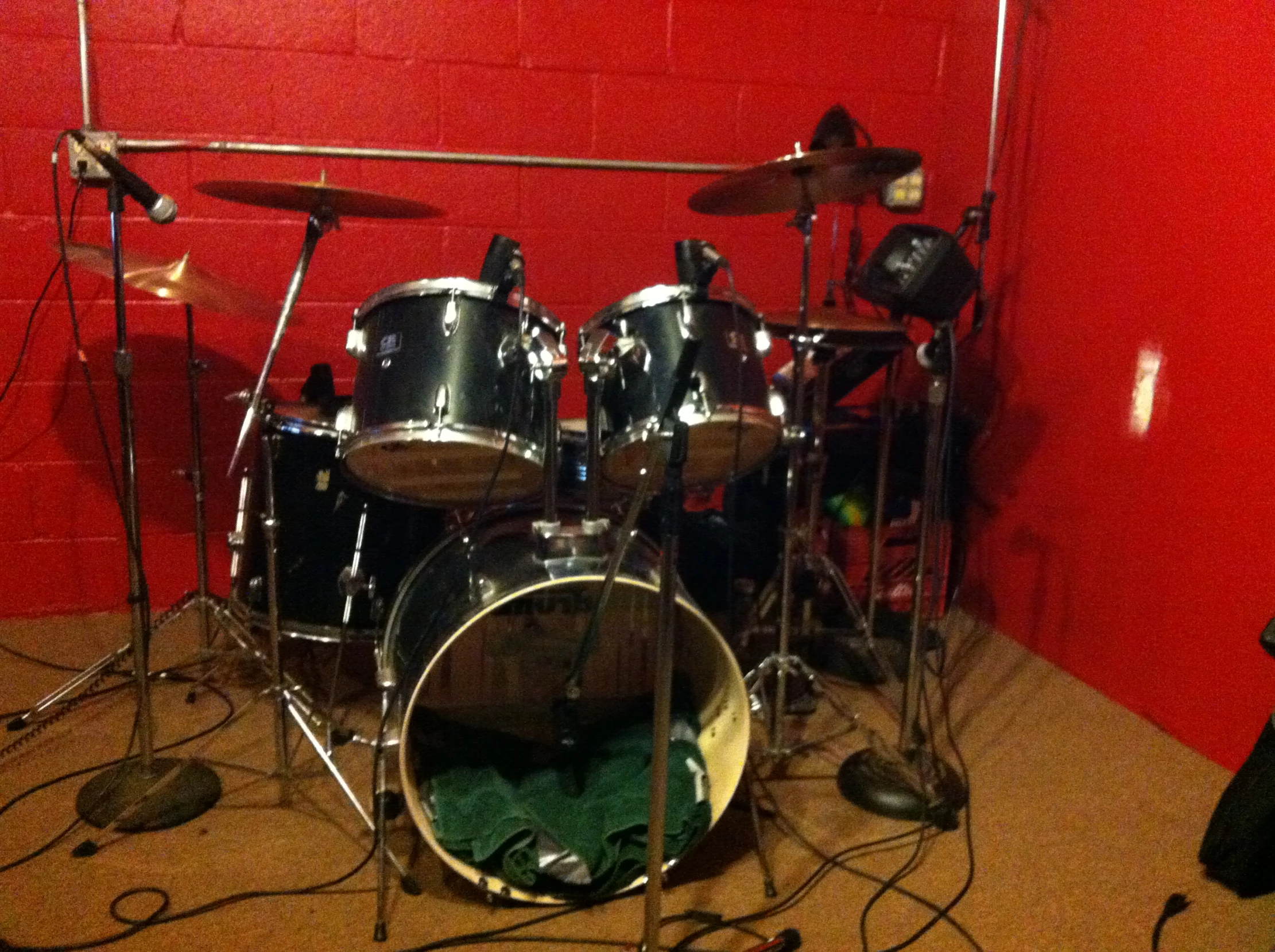 a drum set sits in a red room with microphones