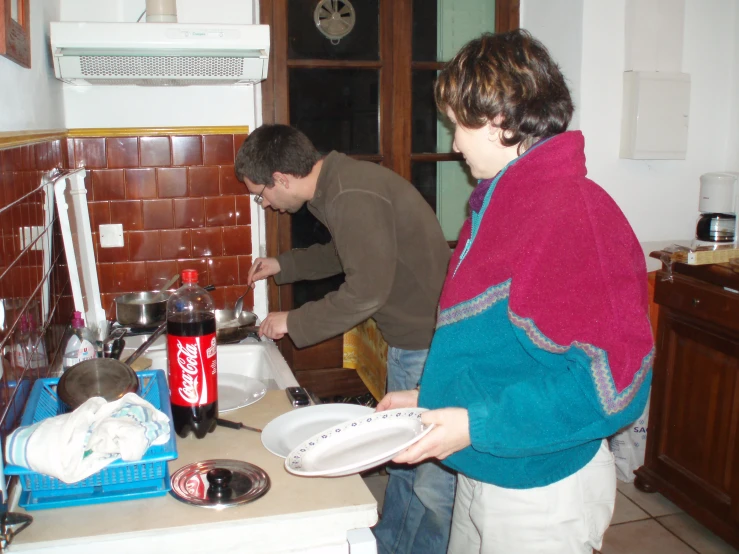 two people prepare food in a kitchen with one holding a plate