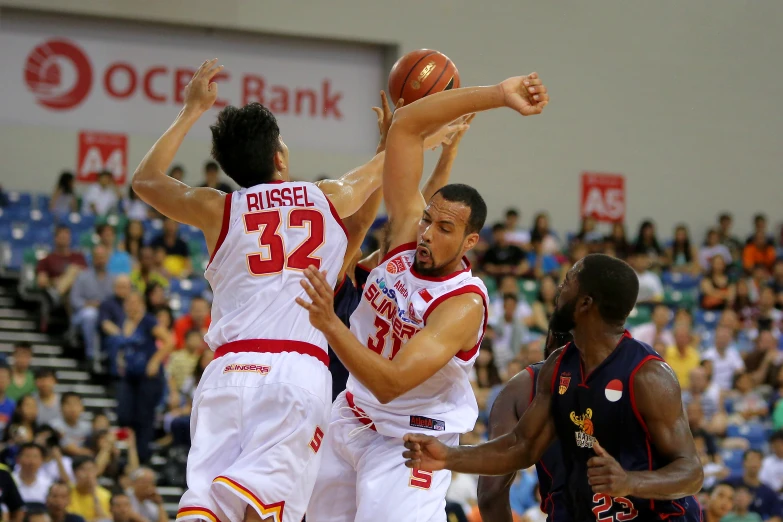 three men playing basketball, one has his foot up as the other tries to block the ball