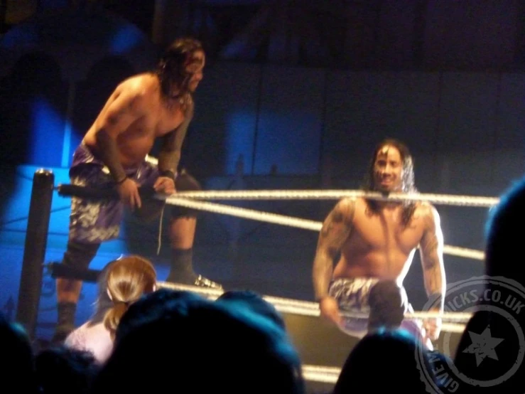 two men in wrestling uniforms are standing on the ropes