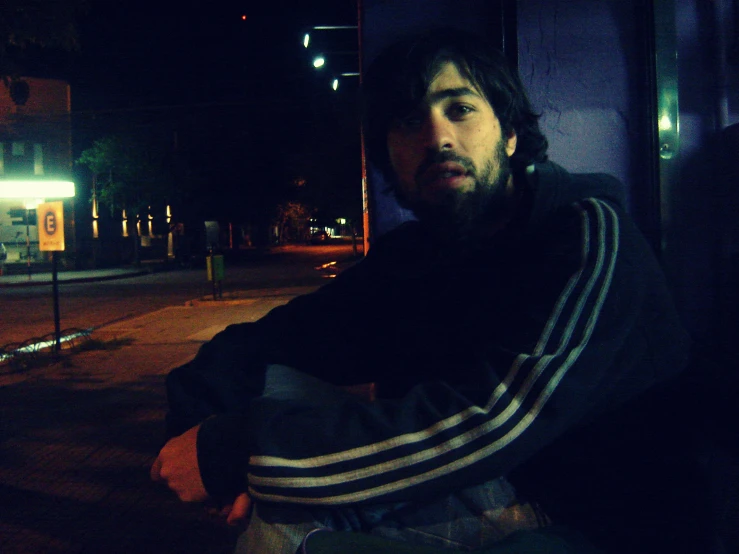 man sitting on the sidewalk at night wearing a hoodie