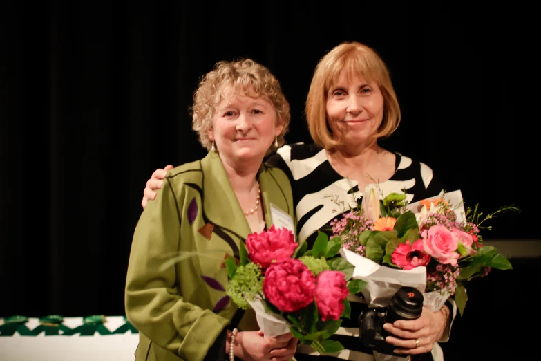 two women stand together with flowers in their hands