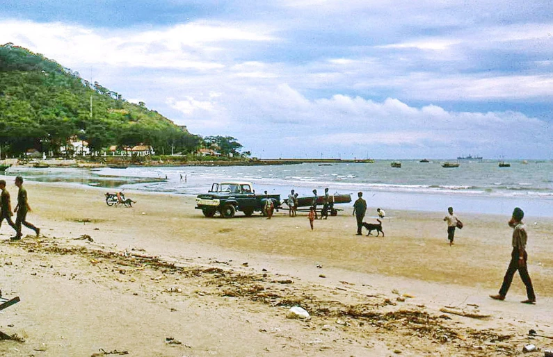 the people are walking on the beach near a hill
