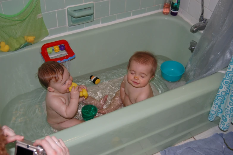 two toddlers in the tub playing with toys