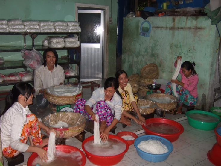 four women making cakes in a bakery with many bowls and buckets on the floor