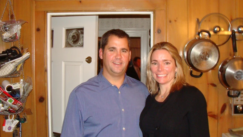 the smiling couple poses for a po in front of some kitchen cooking utensils