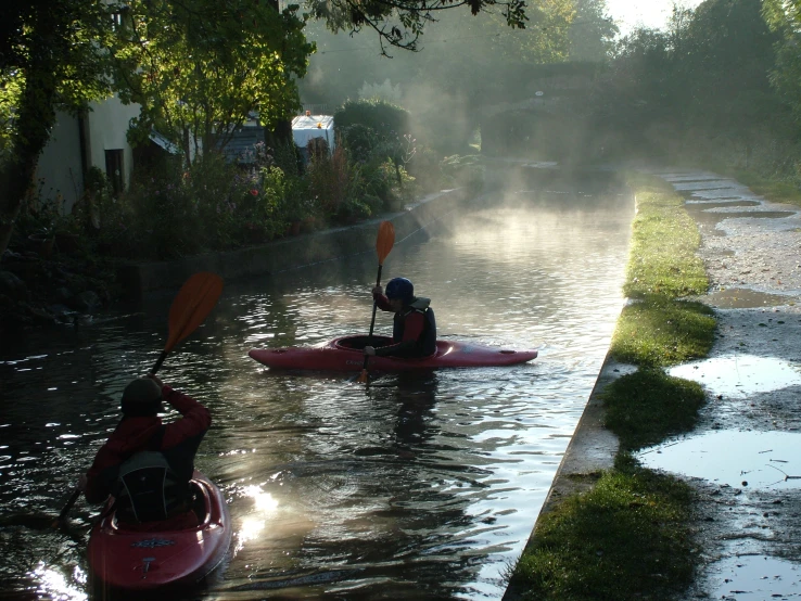 two kayakers paddling down a stream, with mist behind them