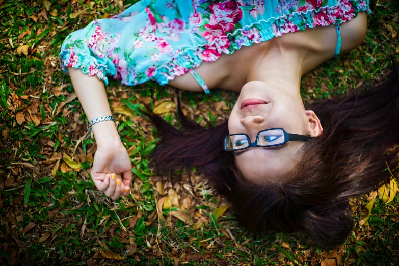 a girl with glasses lays in the grass