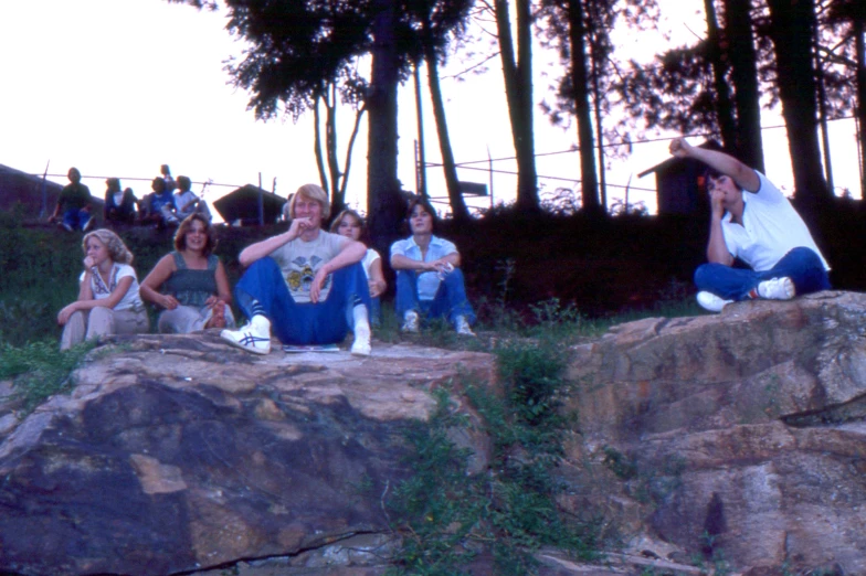 a few women sit on a rock in front of trees