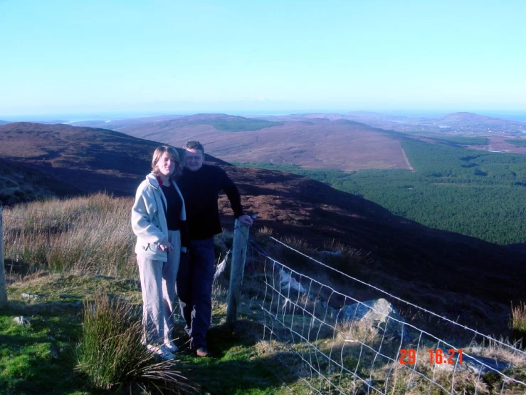 two people stand on the side of a hill near a fence