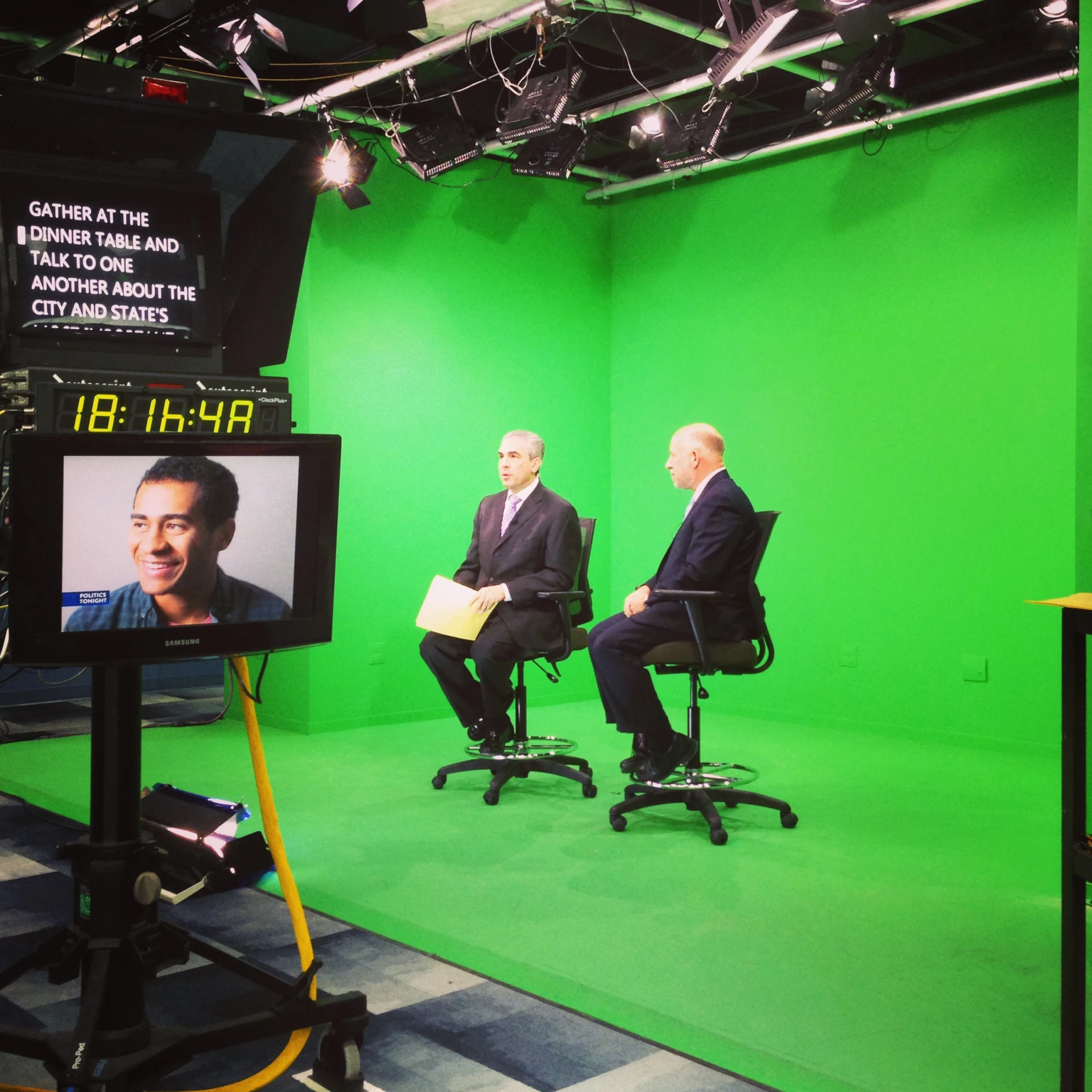 two men sit on chairs in front of green screen